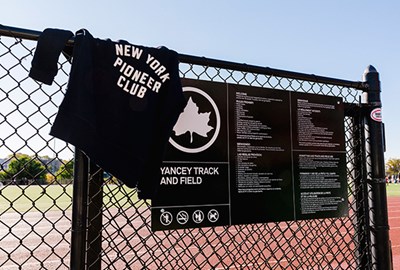 New York Pioneer Club sweatshirt on fence with Yancey Track and Field sign